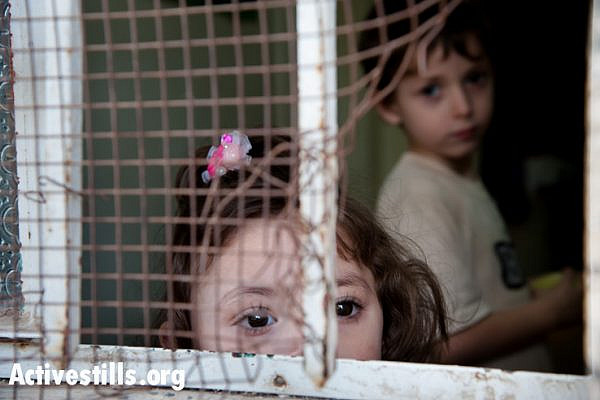 The children of Hashem Al Azzeh look through a window in their house near the Israeli settlement of Tel Rumeida in the West Bank city of Hebron. Their home has been attacked by Israeli settlers on numerous occasions. (Activestills)