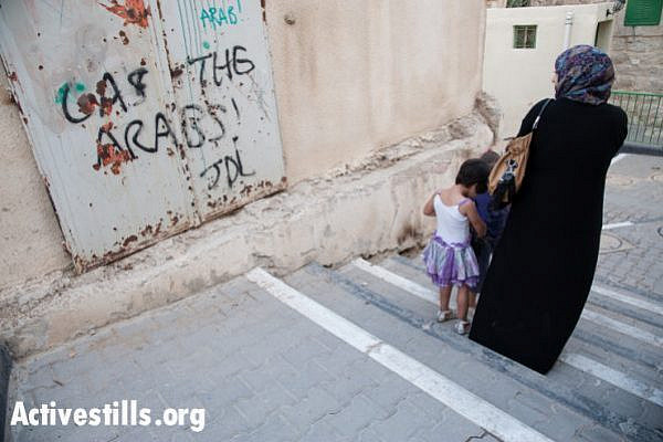 A Palestinian woman and children pass the slogan "Gas the Arabs! JDL" spray-painted on an exterior wall of the Cordoba School for Palestinian children near Shuhada Street, Hebron, October 22, 2012. "JDL" stands for Jewish Defense League, an extremist group founded by Meir Kahane and designated as a terrorist group by the FBI. Baruch Goldstein was a charter member of the JDL, which has designated him "a martyr in Judaism's protracted struggle against Arab terrorism."