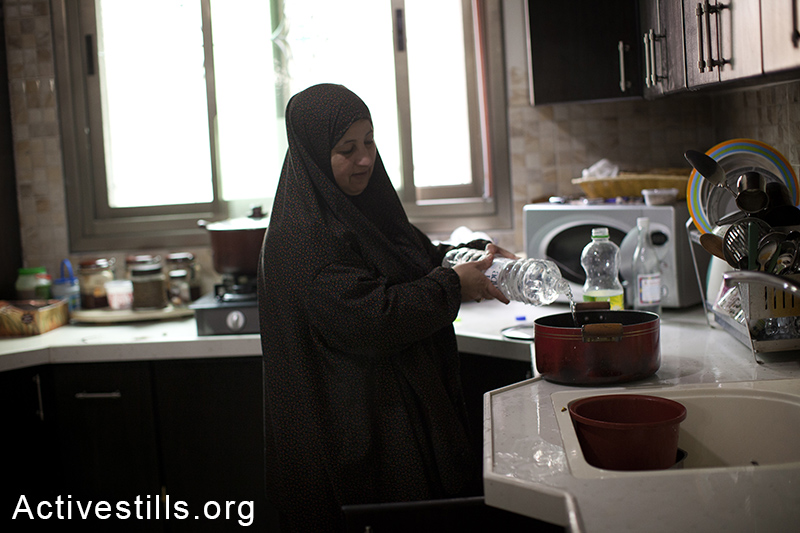 Member of the Swetti family pours water to a put from a plastic bottle, East Jerusalem, March 15, 2014. The family of nine, living in the Ras Shehada neighborhood has been going 10 days without running water. (Activestills.org)