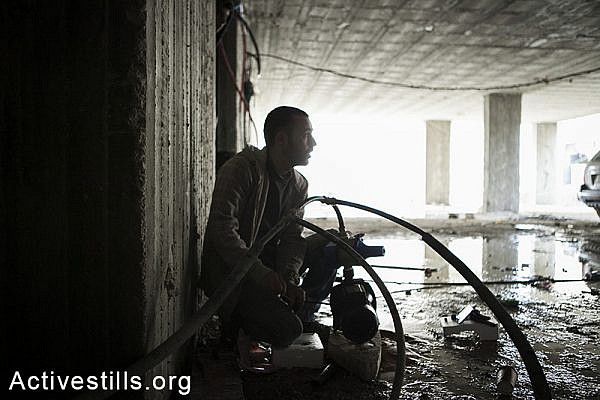 A resident of Ras Shehada plugs the building's pipe to a pump to help the water pressure, East Jerusalem, March 15, 2014. The family of nine, living in the Ras Shehada neighborhood has been going 10 days without running water. (Activestills.org)