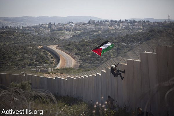 A Palestinian youth places a flag on the Israeli wall during a protest marking 9 years for the struggle against the wall in the West Bank village of Bilin, February 28, 2014. (photo: Oren Ziv/Activestills.org)