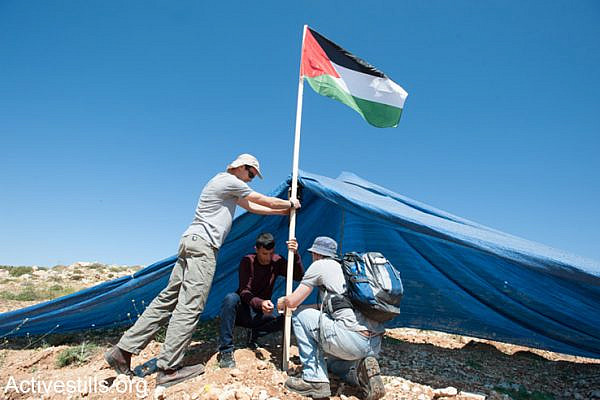 Palestinian and Israeli activists plant a Palestinian flag at a tent placed by settlers on land belonging to the West Bank village of Khirbet An Nahla, April 18, 2014. All Israeli settlements on occupied Palestinian territory are illegal under international law. (Activestills.org)