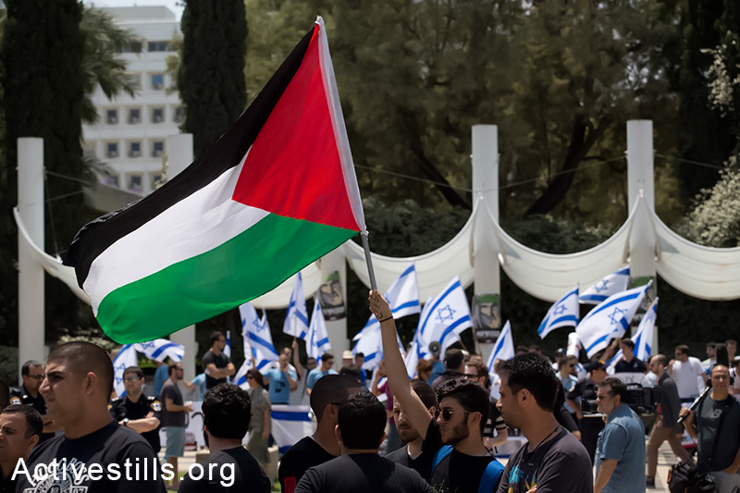 A student raising the Palestinian flag during a ceremony commemorating the Nakba held by Palestinian students living in Israel and Israeli supporters, outside the Tel Aviv university, May 11, 2014. Right-wing nationalists from the "Im Tirzu" group, seen in the back, tried to interrupt the ceremony.