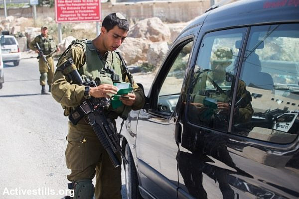 An Israeli soldier checks a Palestinian man’s documents at a checkpoint outside the West Bank city of Hebron on June 17, 2014, as the hunt for three Israeli teenagers believed kidnapped by militants entered its fifth day. (Photo: Tess Scheflan/Activestills.org)