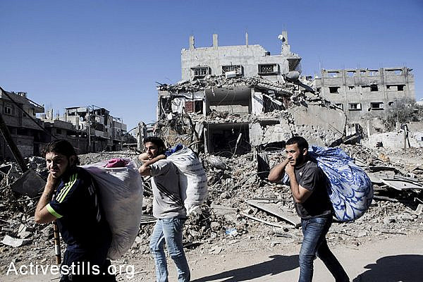 Palestinians walk out with belongings in Shujaiyeh, a neighborhood in the east of Gaza City, during a ceasefire, July 27, 2014. During the ceasefire on 26 July, many Palestinians went back to Shujaiyeh to inspect the damages together with medics who attempted to rescue injured or collect bodies. Dozens of bodies were collected but many remain as Palestinians do not have all the necessary equipment to dig. Israeli attacks turned the neighborhood into a scene of utter devastation, with entire buildings flattened and thousands forced to flee.  Israeli attacks have killed more than 1,000 Palestinians and injured around 5,000 in the current offensive.  (Anne Paq/Activestills.org)
