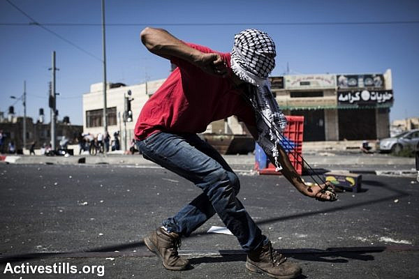 A Palestinian uses a slingshot to throw rocks at Israeli forces in Shuafat refugee camp. Clashes erupted after the body of a Palestinian teenager was found in a Jerusalem forest. (photo: Activestills.org)