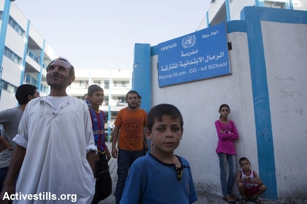 Palestinians stand in front of the entrance of Remal Elementary UNRWA School which is used as a temporary shelter for people from the northern part of the Gaza Strip, Gaza City on July 13, 2014. People from northern Gaza left their homes after Israel dropped leaflets warning them to evacuate. Israeli attacks have killed at least 166 Palestinians, including 30 children. (Photo by Anne Paq/Activestills.org)