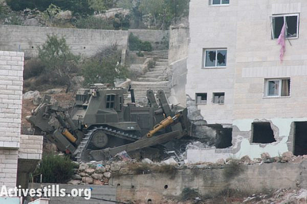 An Israeli military bulldozer destroys part of the family home of Zakaria Al-Aqra, age 24, after he was killed by an army raid in the West Bank village of Qabalan, August 11, 2014.