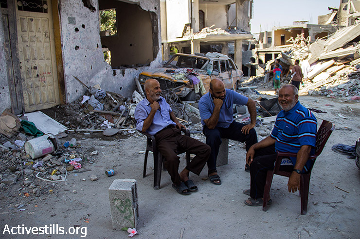 Abu Alaa sits with his neighbours exchanging jokes on the occupation army. August 12, 2014. (Basel Yazouri/Activestills.org)
