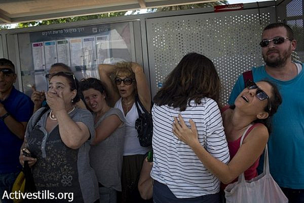 Israelis take cover near a bus stop in a street in center Tel Aviv during a siren alarm as a rocket Is launched from Gaza strip, August 3, 2014. (Oren Ziv/Activestills.org)