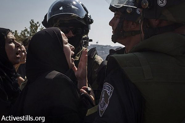 Palestinian women argue with an Israeli soldiers, after a Palestinian youth was shot with live ammunition and was taken by the army, during the weekly protest against the occupation, in the West Bank village of Nabi Saleh, August 15, 2014. (Keren Manor/Activestills.org)