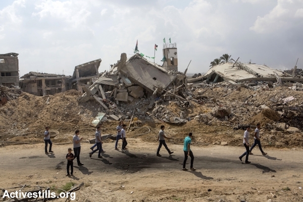 Palestinian school students pass by some destroyed buildings and homes in the Shujaiya neighborhood, Gaza city, September 15, 2014. (Photo by Anne Paq/Activestills.org)