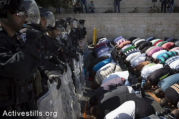 Palestinian Muslim worshipers perform traditional Friday prayers in a street in Wadi Joz neighbourhood outside Jerusalem's Old City, as policemen block their way to Al Aqsa mosque, October 17, 2014. The Israeli government has restricted access to the al-Aqsa mosque compound, Islam's third holiest shrine to men under 50. (Activestills.org)