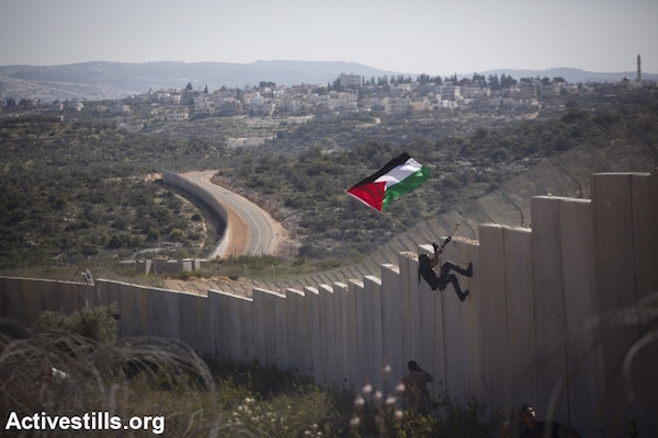 A Palestinian youth places a flag on the Israeli wall during a protest marking nine years of struggle against the wall in the West Bank village of Bilin, February 28, 2014. (Photo by Oren Ziv/Activestills.org)