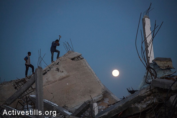 Palestinians salvage materials from destroyed homes at night in the village of Khuza’a, eastern Gaza Strip, November 6, 2014. (Anne Paq/Activestills.org)