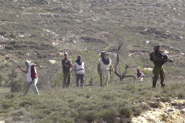 Israeli soldiers accompany settlers as they throw stones toward the Palestinian village of Urif, November 18, 2014. (Screenshot: Yesh Din)