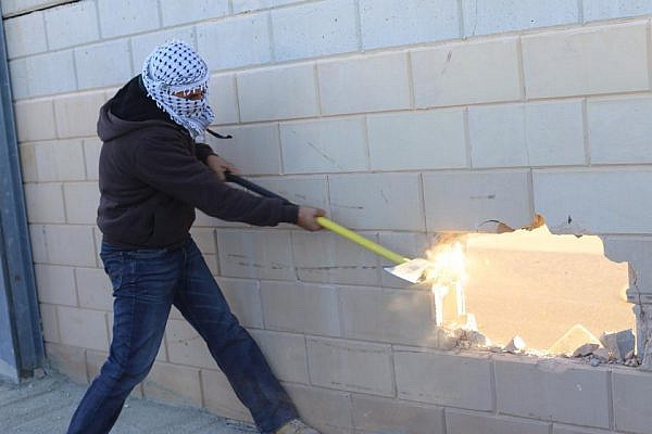 A Palestinian smashes a hole through the separation wall near Jerusalem. (photo: Popular Struggle Coordination Committee)