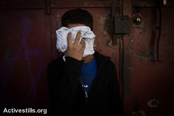 A Palestinian youth cover his face to avoid tear gas, during clashes of Palestinian youth with Israeli border police at a checkpoint between Shuafat refugee camp and Jerusalem, November 7, 2014. Clashes broke after a Palestinian man drove a car into a crowd, killing a policeman and injuring 13 people in Jerusalem on November 5. (photo: Activestills.org)