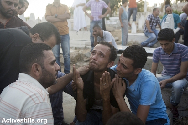 A relative of a child killed earlier in a playground in al-Shati refugee camp mourns at a cemetery, Gaza City, July 28, 2014. Reports indicated that 10 people, mostly children, were killed and 40 injured during the attack which took place on the first day of the Muslim holiday of Eid. (Photo by Anne Paq/Activestills.org)