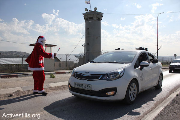 A Palestinian man dressed as Santa Claus hands out flowers cars passing through the Huwwara military checkpoint, south of Nablus, during a protest against Israeli occupation, January 1, 2015. One protester was arrested during the action. (Photo by Ahmad Al-Bazz/Activestills.org)