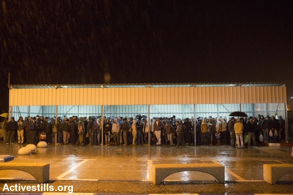 Palestinians holding Israeli work permits take cover from the rain as they wait to cross into Israel before dawn in order to make it to their workplaces, Eyal Checkpoint near Qalqilya, January 4, 2015. (Photo by Oren Ziv/Activestills.org)