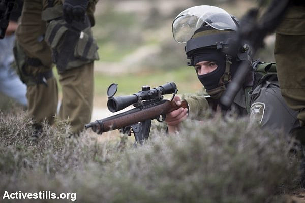 An Israeli solider with a Ruger riffle lies on the ground during a demonstration commemorating the death of Palestinian minister, Ziad Abu Ein, in the West Bank village of Turmus Ayya, north of Ramallah, December 19, 2014. (photo: Oren Ziv)