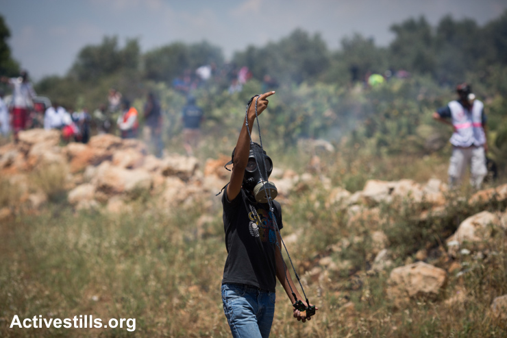 A Palestinian youth gestures toward Israeli soldiers during a protest against the Israeli Separation Wall on Nakba Day, Nil'in, West Bank, May 15, 2015.