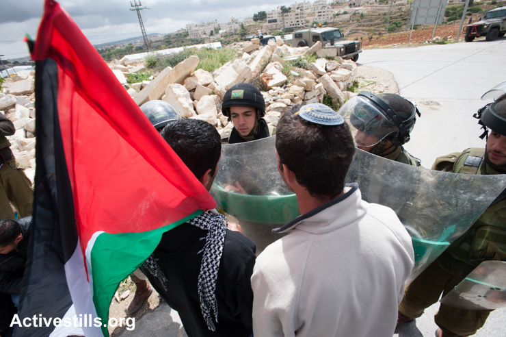 A Palestinian and a Jewish Israeli activist confront heavily armed Israeli soldiers during a weekly demonstration against the occupation and separation wall in the West Bank village of Al Ma'sara, April 5, 2013. (photo: Ryan Rodrick Beiler/Activestills.org)