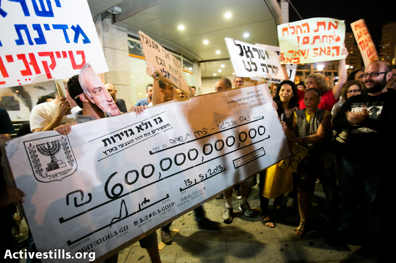 Protesters hold a sing of a check from the state of Israel to Yitzhak Tshuva with the estimated value of natural gas during demonstration against privatization of natural gas found in the Mediterranean sea. protesters marched to the house of energy minster silvan shalom on may 11, 2013. (Yotam Ronen/Activestills.org) 