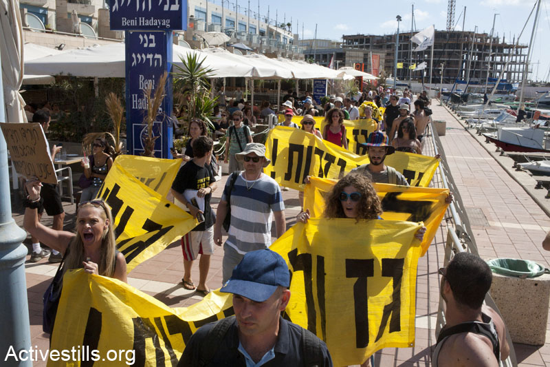 Activists march in Herzliya marina, calling on passersby to not support the Israeli government in its bid to privatize the natural gas found in the Mediterranean sea. The march took place after a protest flotilla left Herzliya shore and sailed a few kilometers out to sea, escorted by other supporters on boats, June 15, 2013. (Keren Manor/Activestills.org) 