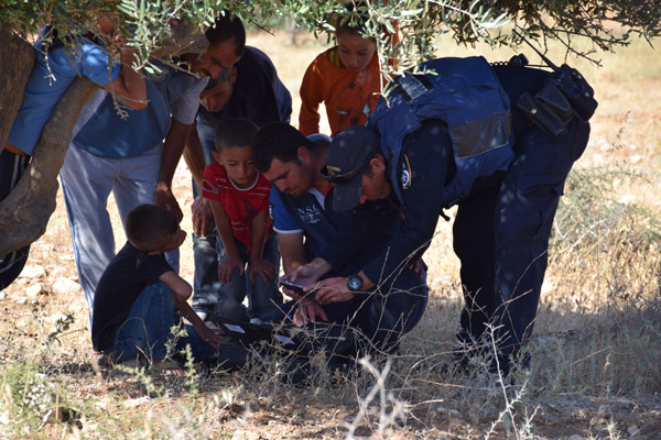 An Israeli police officer films video of settlers throwing stones, being shown to him by Nasser under an olive tree just meters from where the incident took place, June 13, 2015. (Photo by Michael Schaeffer Omer-Man)