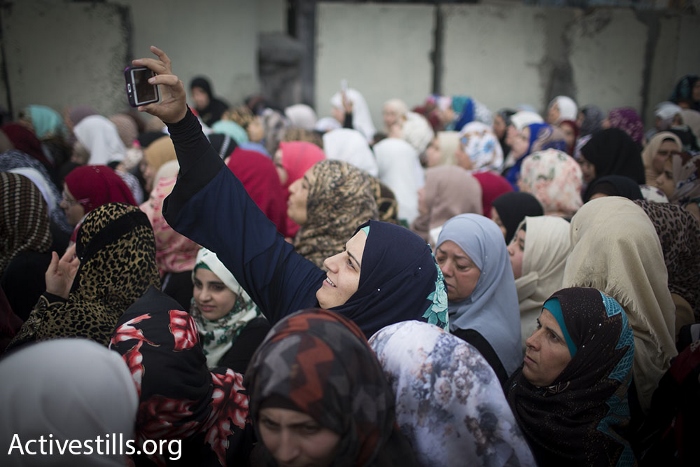 A Palestinian woman takes a 'selfie' while standing in line at Qalandiya checkpoint during the second Friday of Ramadan, June 26, 2015. (photo: Oren Ziv/Activestills.org)