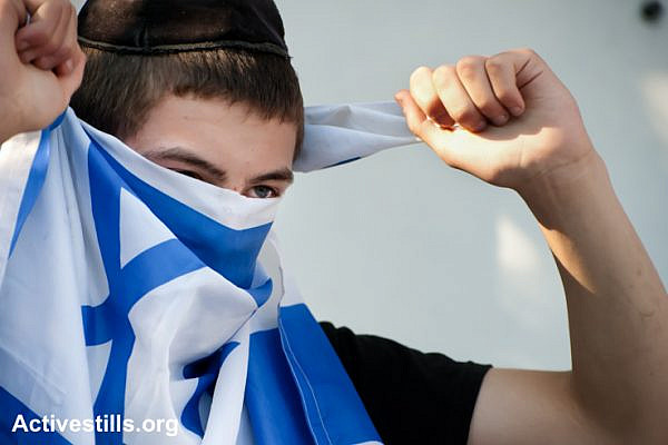 An Israeli settler youth living in a confiscated Palestinian home in the East Jerusalem neighborhood of Sheikh Jarrah covers his face with the Israeli flag, September 2, 2011. (photo: Ryan Rodrick Beiler/Activestills.org)