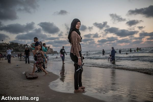 A Palestinian woman stands in the Mediterranean Sea during the last day of the Eid al-Fitr holiday as the sun sets in Tel Aviv, Israel, Sunday, July 19, 2015. Israeli authorities issued thousands of permits for Palestinians living in the West Bank, allowing them to visit Israel during the three-day holiday that marks the end of the holy fasting month of Ramadan. (photo: Yotam Ronen/Activestills.org)
