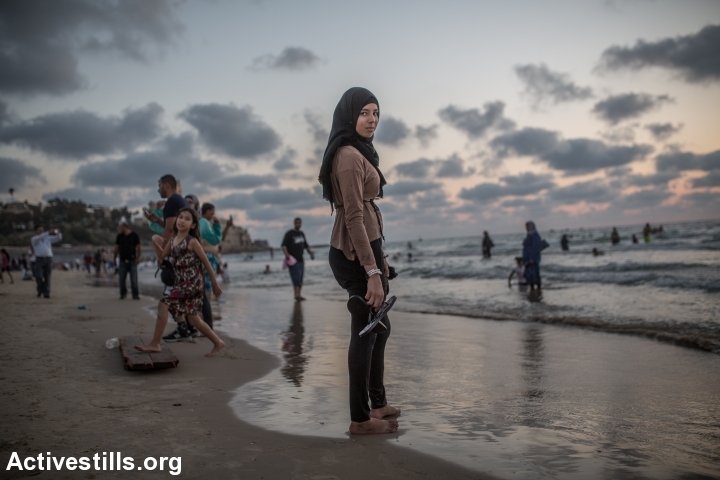 A Palestinian woman stands in the Mediterranean Sea during the last day of the Eid al-Fitr holiday as the sun sets in Tel Aviv, Israel, Sunday, July 19, 2015. Israeli authorities issued thousands of permits for Palestinians living in the West Bank, allowing them to visit Israel during the three-day holiday that marks the end of the holy fasting month of Ramadan. (photo: Yotam Ronen/Activestills.org)
