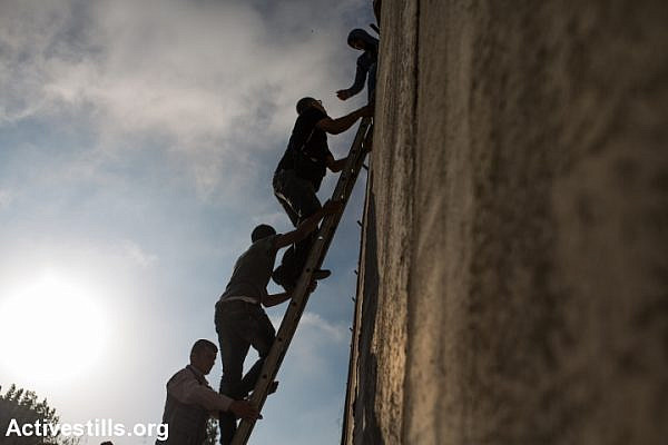 Palestinians climb over the Israeli Wall to attend the Friday prayer in Al-Aqsa Mosque, in the town of Al-Ram, near the Qalandiya checkpoint between the West Bank city of Ramallah and Jerusalem, on the second Friday of the Muslim holy month of Ramadan, July 3, 2015. (Yotam Ronen/Activestills.org)