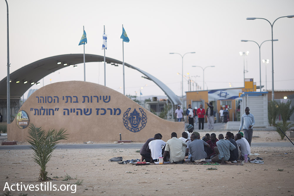 Sudanese asylum seekers sit in groups outside the gates of the Holot detention facility while they wait for the daily Ramadan fast to end, July 2015. (Oren Ziv/Activestills.org)