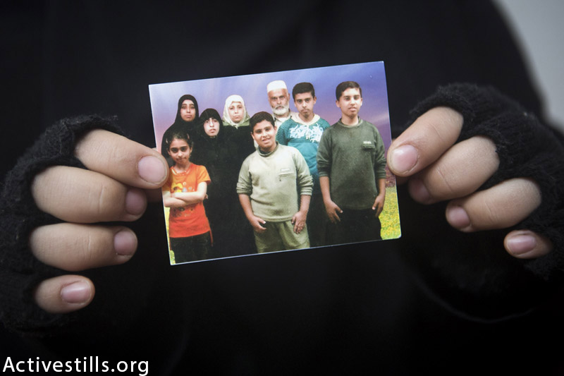 Photo of the Al Haj family held by Fida'a al Haj in their temporary home, in Khan Younis refugee camp, February 18, 2015. Only two members featured on the photo  -Yasser (26) and his sister Fida'a (27)  are still alive, as 8 members- Mahmoud, his wife and 6 of their children- were killed by an Israeli attack on their home on 10 July 2014. Yasser was visiting friends and witnessed the attack while Fida'a was staying with her husband's family. (Anne Paq / Activestills.org) 