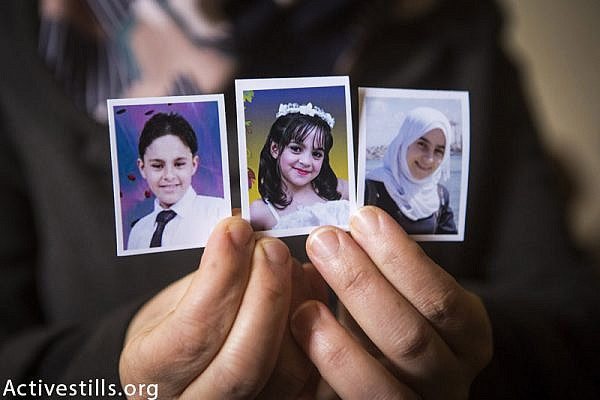 Photos (from left to right) of the killed siblings Mohammed (12), Yara (8) and Nadeen (16) Mahmoud Al Farra, held by their mother in their home in Khan Younis, February 22, 2015. 9 members of the Al Farra family were killed in the street by an Israeli missile while they were fleeing their home after it was attacked on August 1st, 2014. (Anne Paq / Activestills.org)
