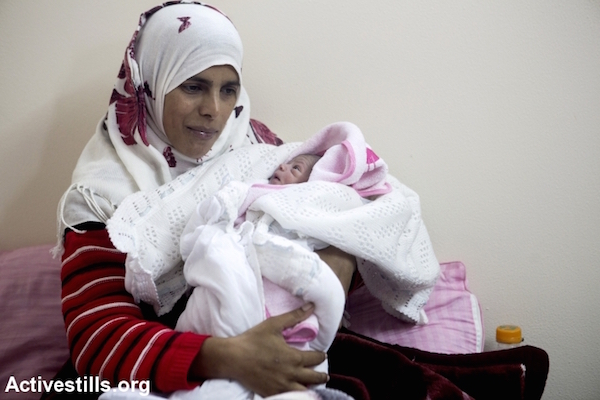 A mother with her newborn daughter in a displaced persons' camp in Khuza'a, Gaza Strip, November 7, 2014. (Anne Paq/Activestills)