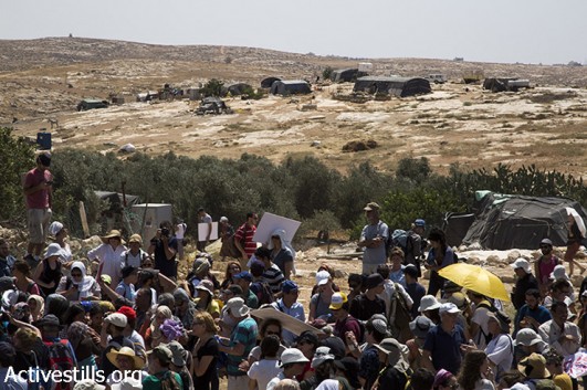 Palestinian, Israeli and international activists march next to the village of Susiya to protest its imminent demolition and the forced transfer of its residents, South Hebron Hills, West Bank, July 24, 2015. The activists marched through the village, stopping at various homes along their way to hear the stories of families facing eviction and transfer. At the end of the demonstration activists hung a massive banner in view of passing settlers, declaring that Susiya is here to stay. (photo: Keren Manor / Activestills.org)