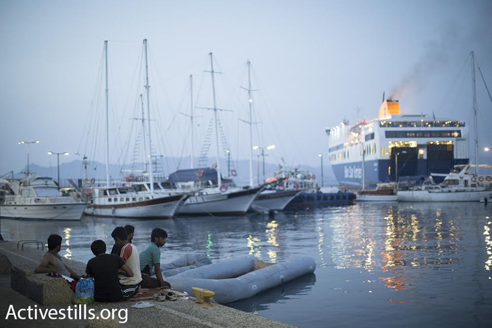 Afghani refugees sit at the Kos port, watching a ship carrying Syrian refugees and tourists, Kos, Greece, September 9, 2015. (photo: Oren Ziv/Activestills.org)