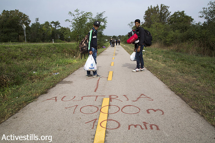 Refugees look at spray painted information indicating the distance to the border. (Keren Manor/Activestills.org)