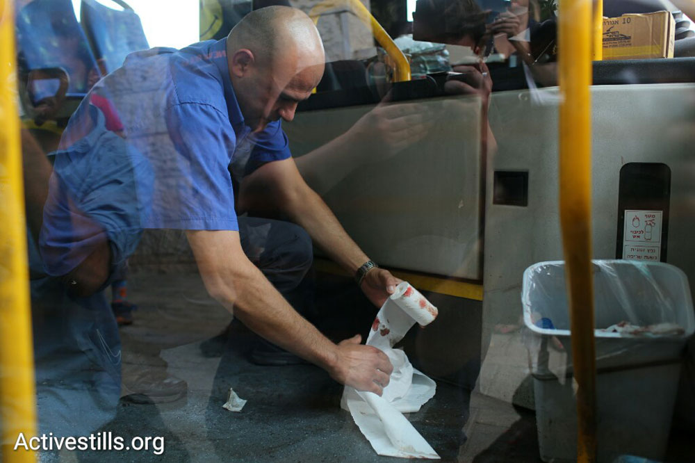 An Israeli bus driver uses toilet paper to clean blood from the entrance of his bus following a stabbing attack, Jerusalem, October 12, 2015. (Oren Ziv/Activestills.org)
