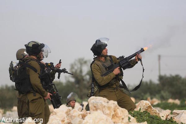 An Israeli solider shoots tear gas toward Palestinian demonstrators during a protest against the occupation in the West Bank village of Budrus, three days after soldiers shot and killed 16-year-old Samir Awad, January 18, 2013. (Oren Ziv/Activestills.org)