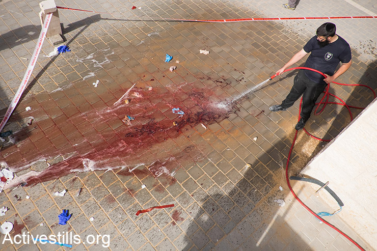 An ultra-orthodox Jew cleans the site where two Palestinians were shot by the Israeli police, after an alleged stabbing attack on an Israeli, in the city of Beit Shemesh, west of Jerusalem, October 22, 2015. (Activestills.org)