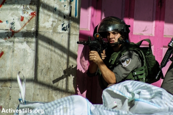 An Israeli Border Police officer prepares to shoot toward protesters after the funeral of Hadeel al-Hashlamon, who was shot and killed by Israeli soldiers, September 23, 2015. (Mohannad Darabee/Activestills.org)