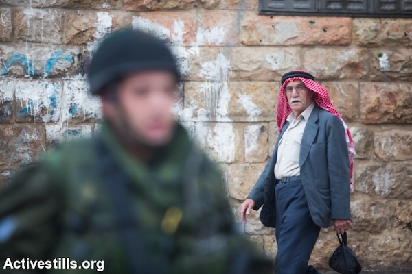 A elderly Palestinian man walks past an Israeli soldier stationed in the center of the occupied city of Hebron, West Bank, October 29, 2015. (Yotam Ronen/Activestills.org)