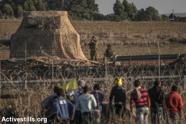 An Israeli soldier raises his rifle toward unarmed Palestinian protesters along the border fence separating Israel and Gaza, Gaza Strip, near the Nahal Oz crossing, October 30, 2015. (Ezz Zanoun/Activestills.org)