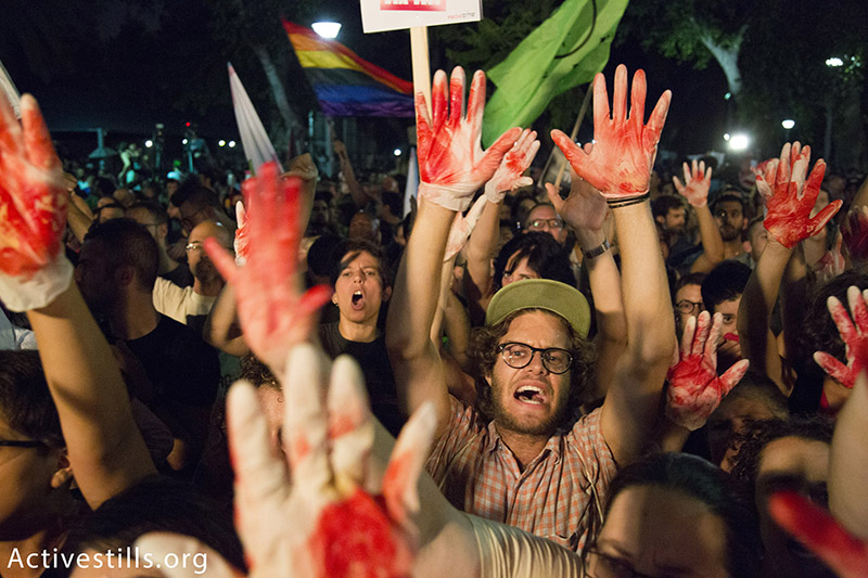 Israeli protesters wave red-painted hands and calling against racist and homophobic propaganda disseminated by Israeli government officials and members of Knesset during their speeches in protest against racism and homophobia, Tel Aviv, Israel, August 1, 2015. Protests were held tonight in Tel Aviv, Jerusalem, Haifa, Beer Sheva and Gan Shmuel Junction, following recent deadly attacks on the Dawabsha family and the stabbing attack in annual Jerusalem Pride Parade.  Activestills.org
